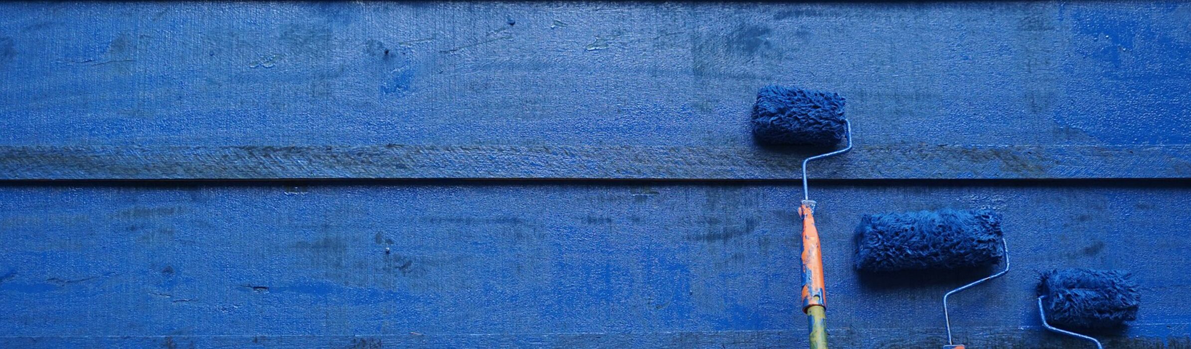 Blaue Holzwand mit Farbrollen